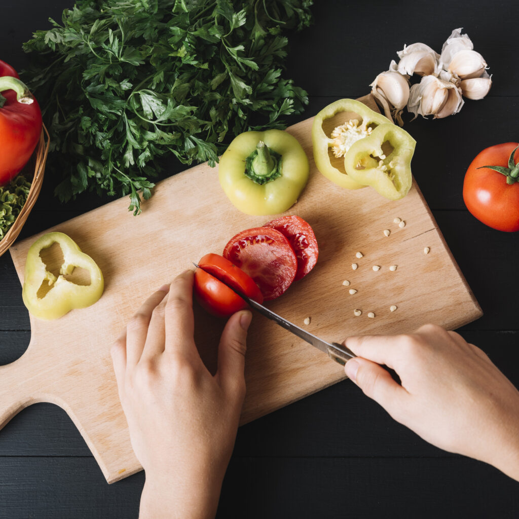 elevated view human hand slicing fresh red tomato wooden chopping board