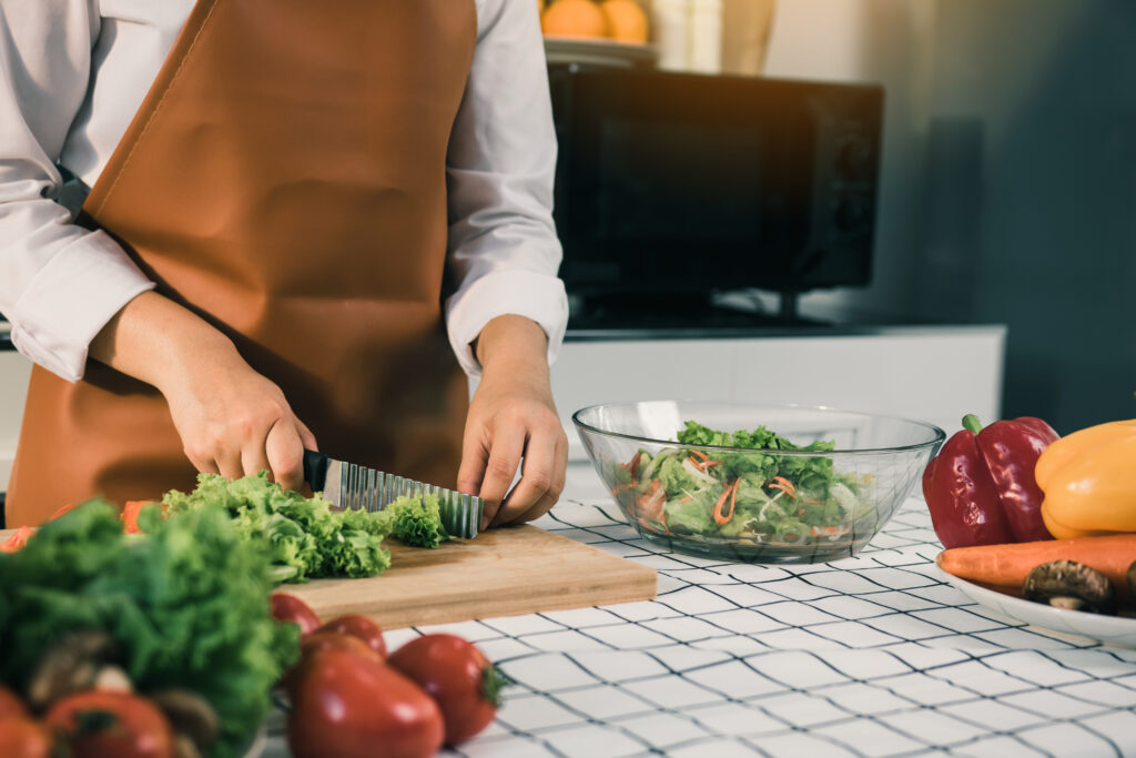 asian woman uses a knife to cut the salad greens in the kitchen.