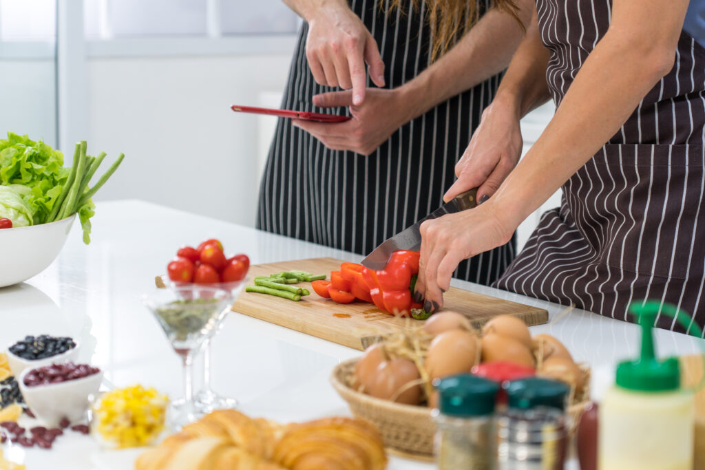 young caucasian woman chopping vegetable while husband using tab