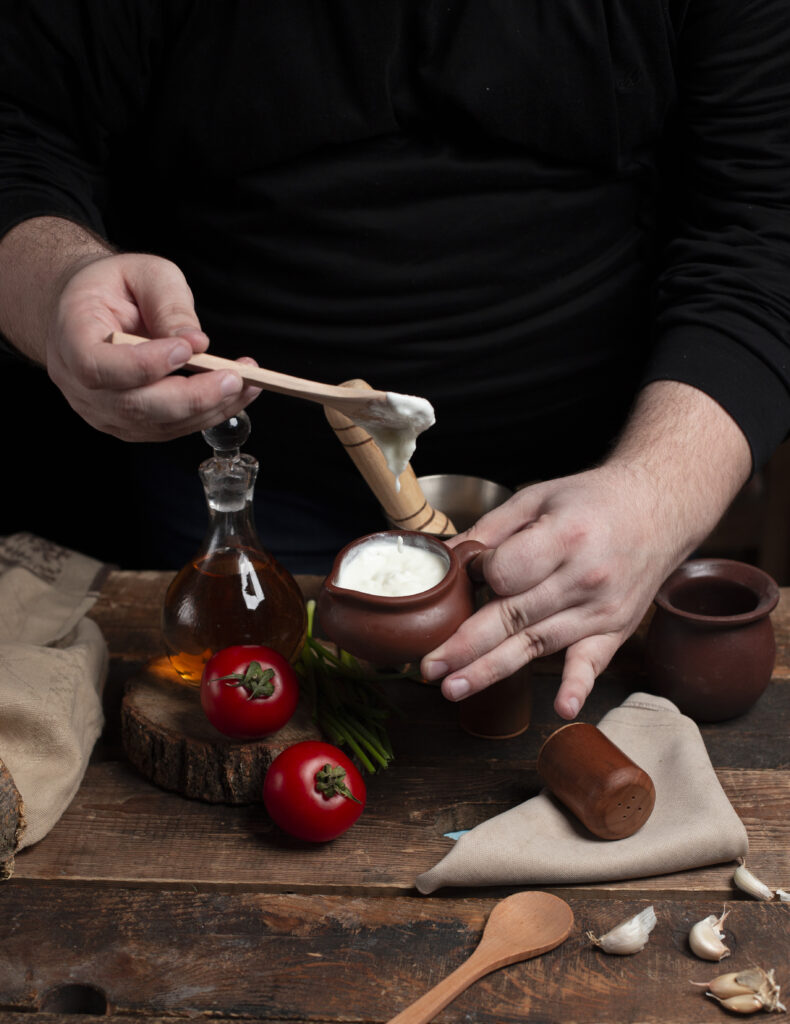 person holding yogurt pot hands tomatoes wooden table